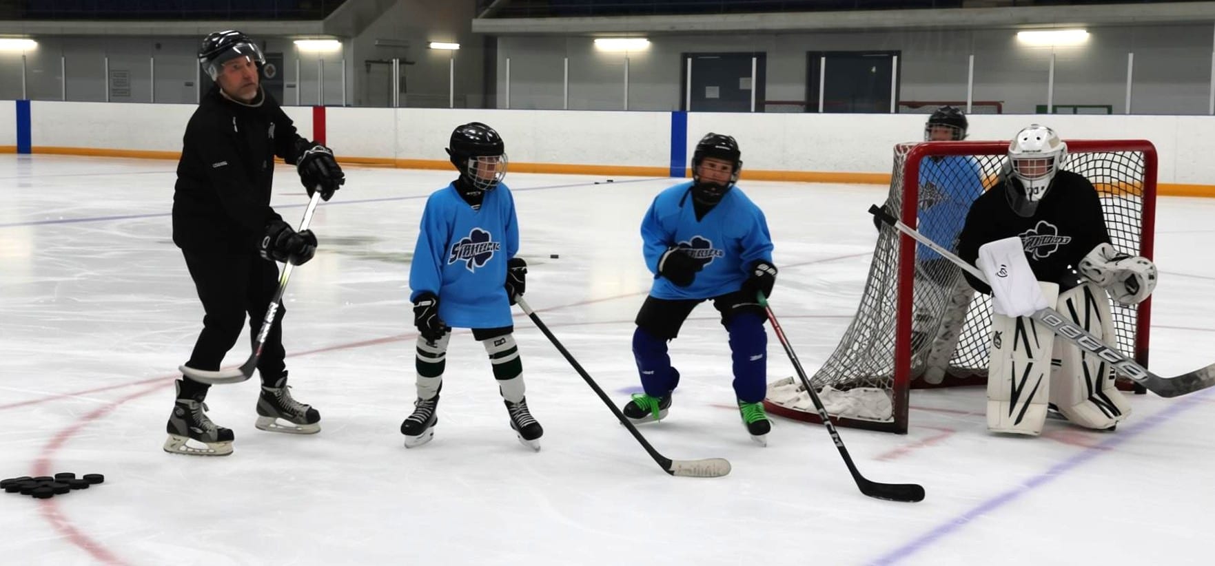 Jesse demonstrating a shot while two players and a goalie work in front of the net