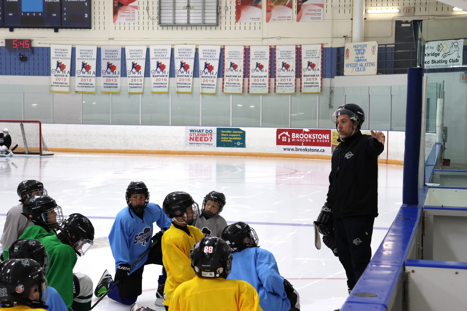 Jesse explaining a drill to a group of players kneeling on the ice